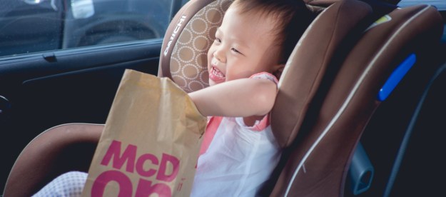 A toddler reaching into a bag of fast food in the car