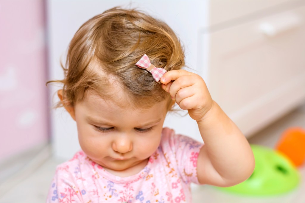 A little girl pulling at her hair clip.