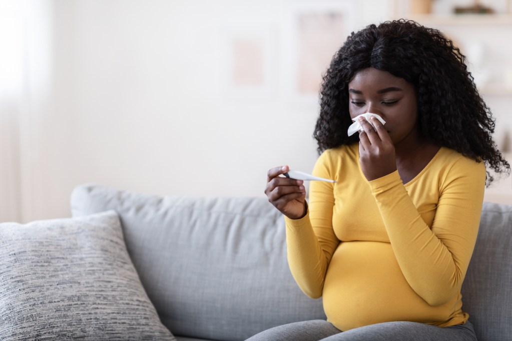 A pregnant woman blowing her nose with a cold.