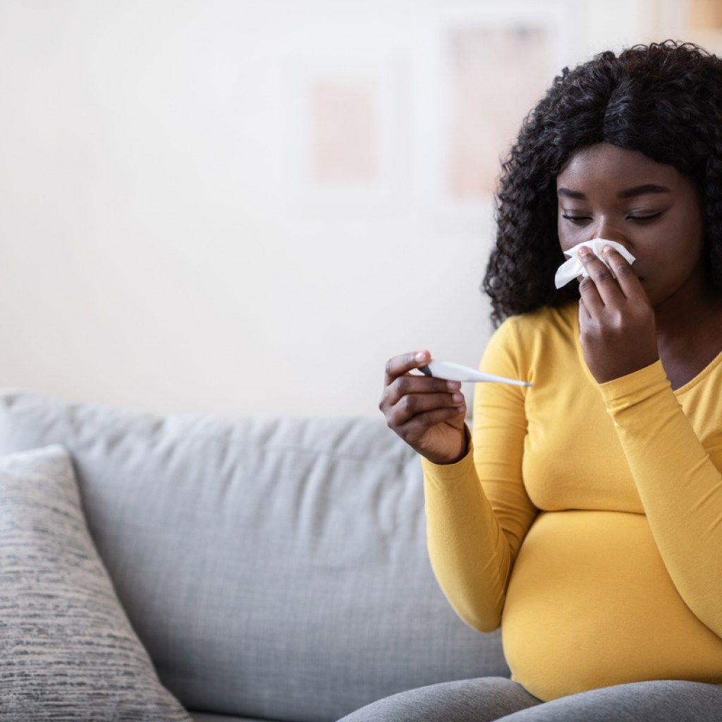 A pregnant woman blowing her nose with a cold.