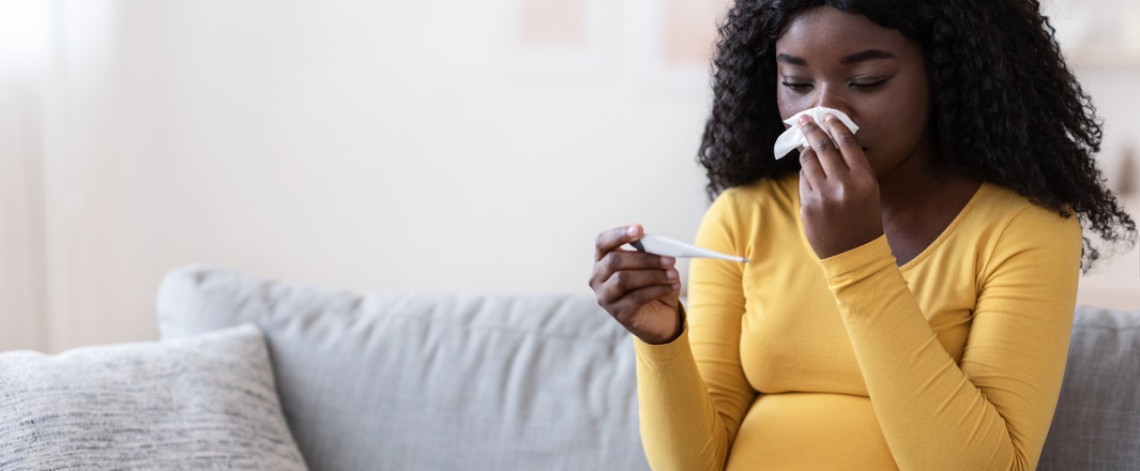 A pregnant woman blowing her nose with a cold.