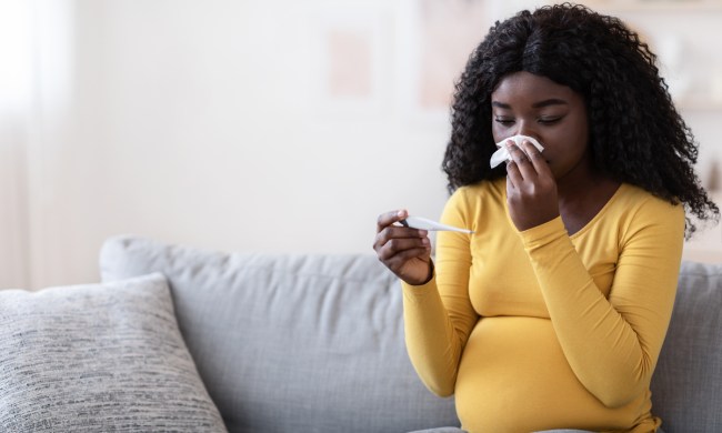 A pregnant woman blowing her nose with a cold.
