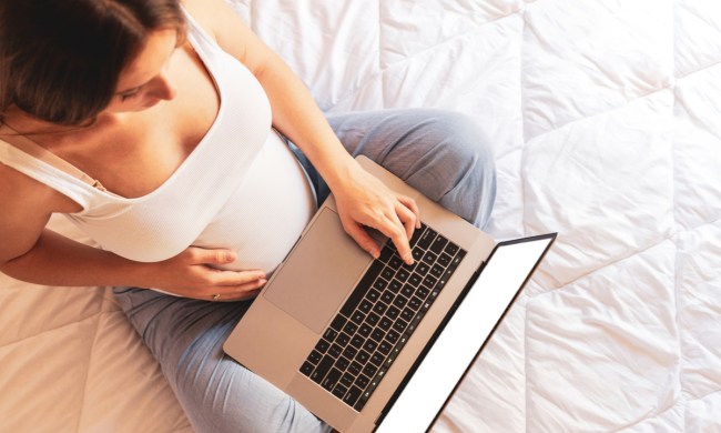 A pregnant woman holding a laptop in her lap while holding her belly