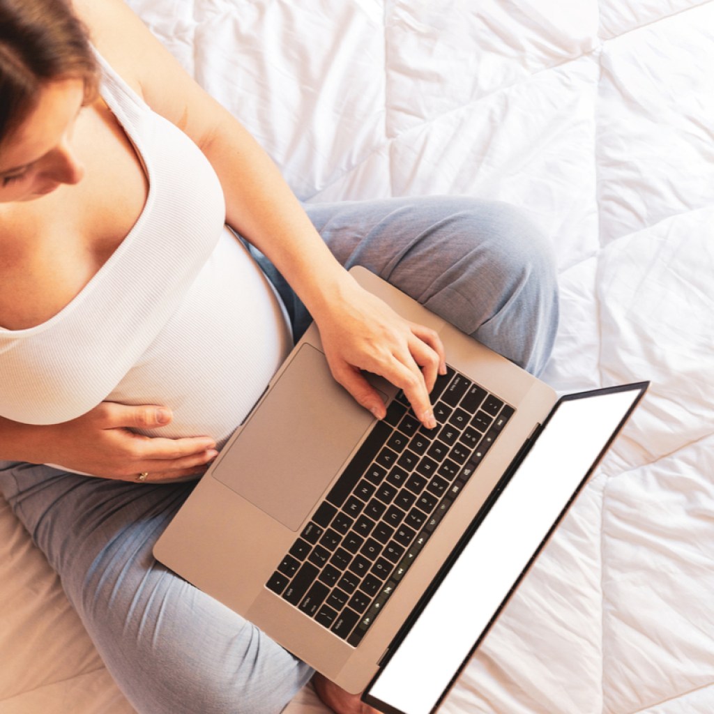 A pregnant woman holding a laptop in her lap while holding her belly.