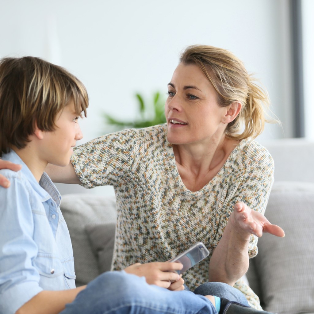 A mother talking to her teenage son while sitting on the couch.