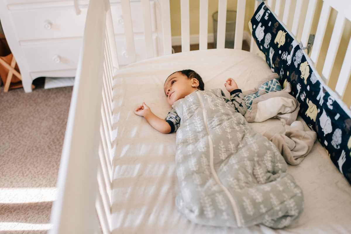 A baby awake in their crib in a sleep sack