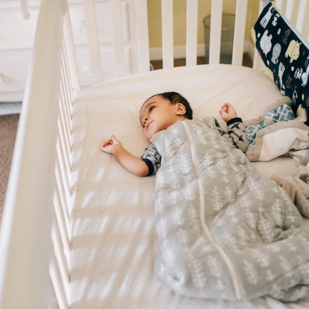 A baby awake in their crib in a sleep sack