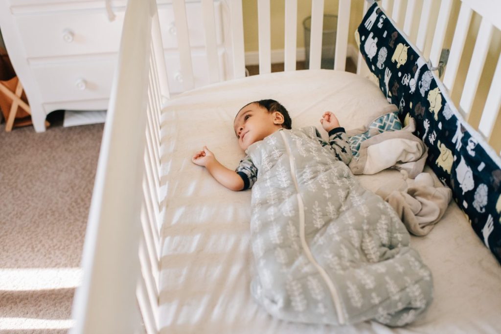 A baby awake in their crib in a sleep sack.
