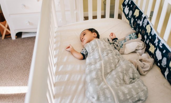 A baby awake in their crib in a sleep sack