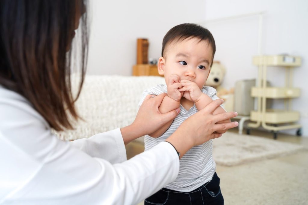 A mother taking her baby's hands out of their mouth.