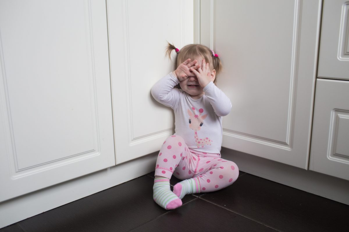 An upset toddler child sitting on the floor in the kitchen.