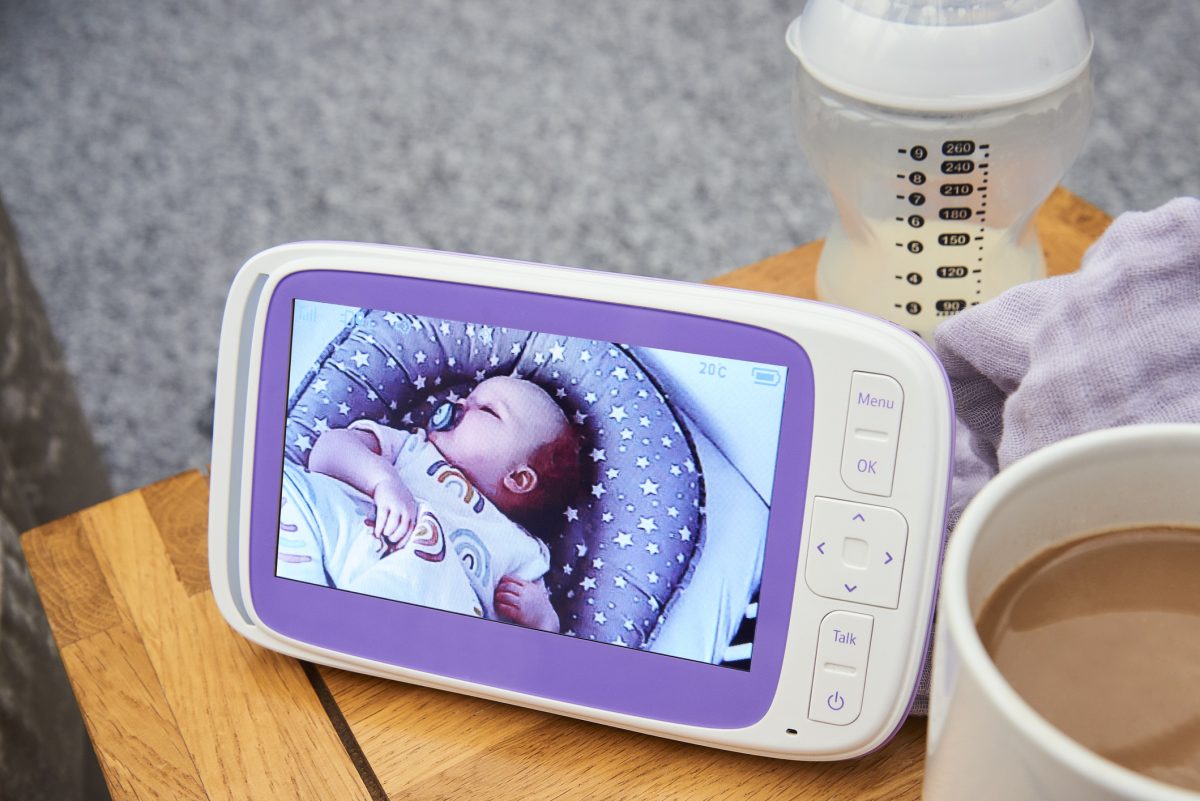 A baby monitor video sitting on a side table by a bottle and cup of coffee