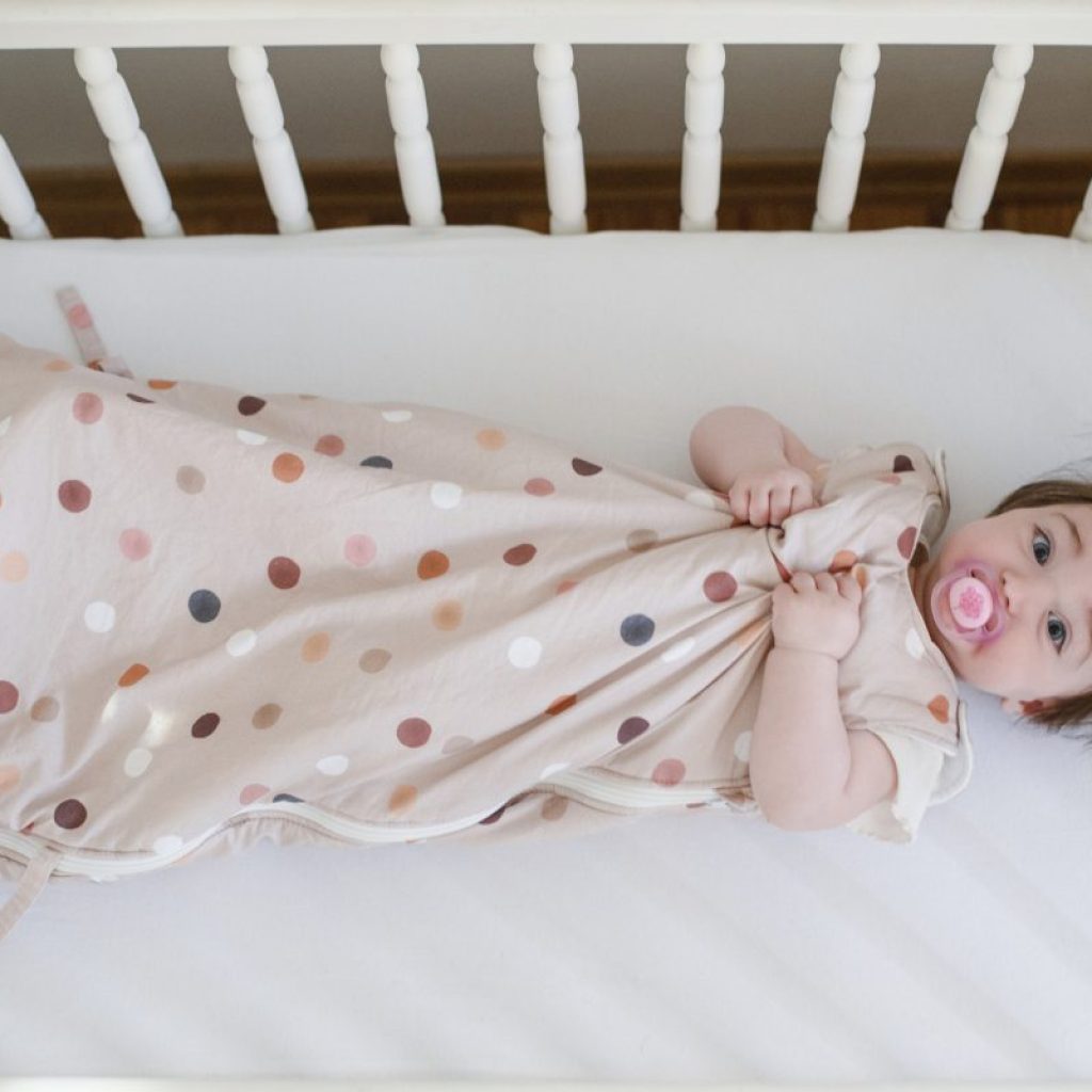 A baby in a sleep sack in their crib.