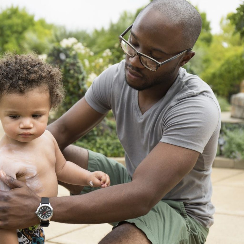 A father putting sunscreen on the body of his young child.
