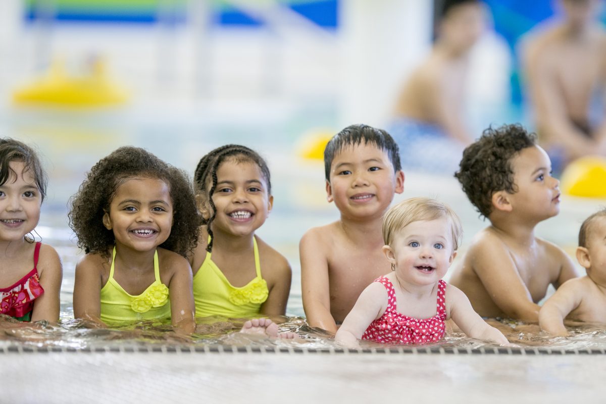 A group of young kids taking a swimming class.