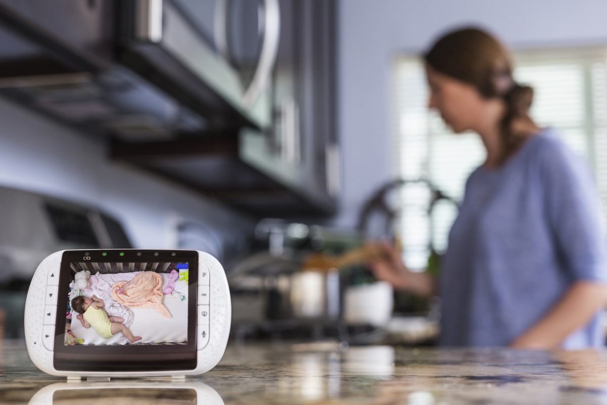 A woman cooking in the background with a baby monitor video in the forefront