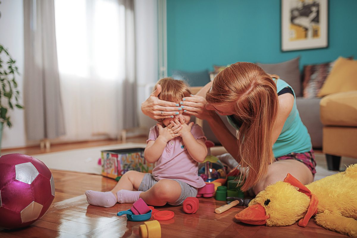 Mother playing peekaboo with her small child.