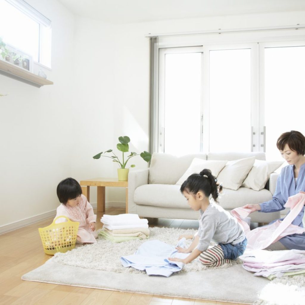 A mother and two young children folding laundry on the living room floor