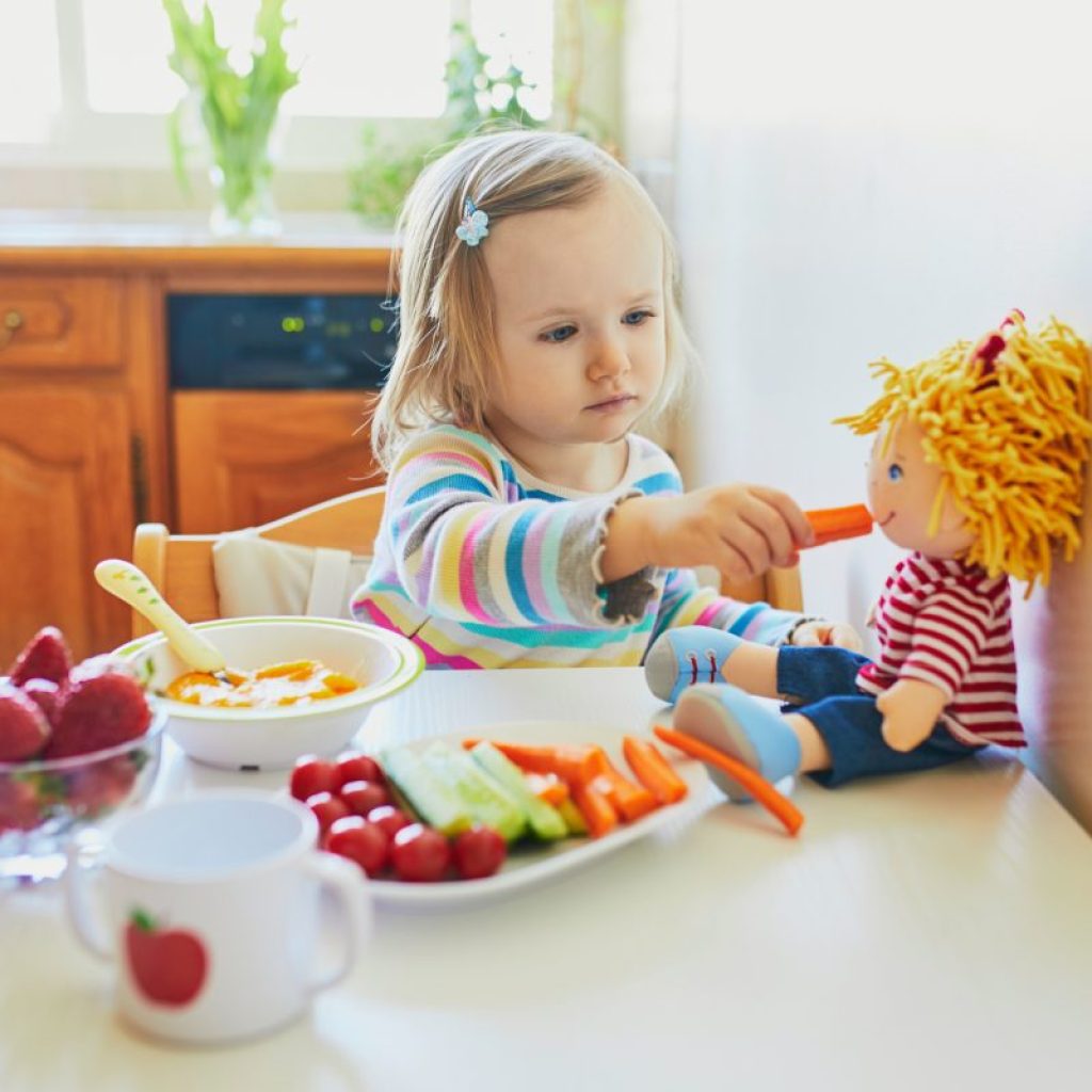 A little girl feeding her food to her toy