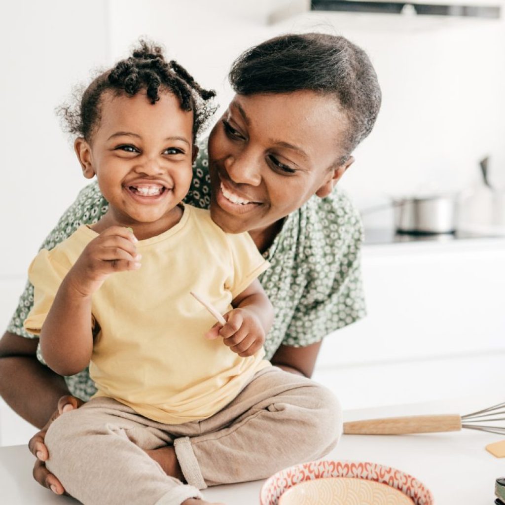 A toddler sitting on the counter while the parent hugs them with prepped food on the counter