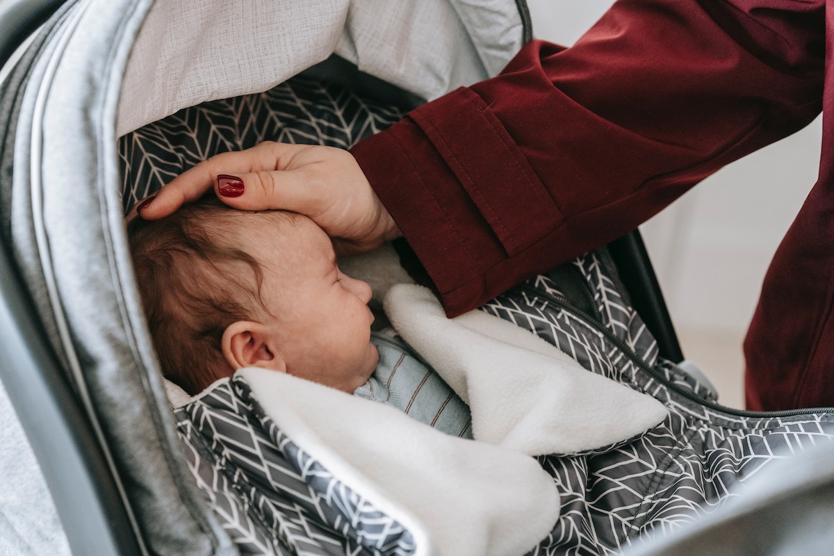 Newborn asleep in stroller with mom patting head