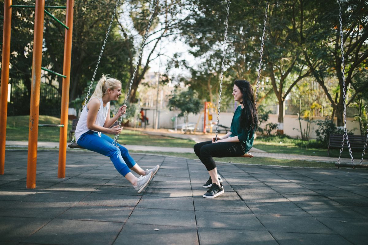 Two friends hanging out on the swings at a park.