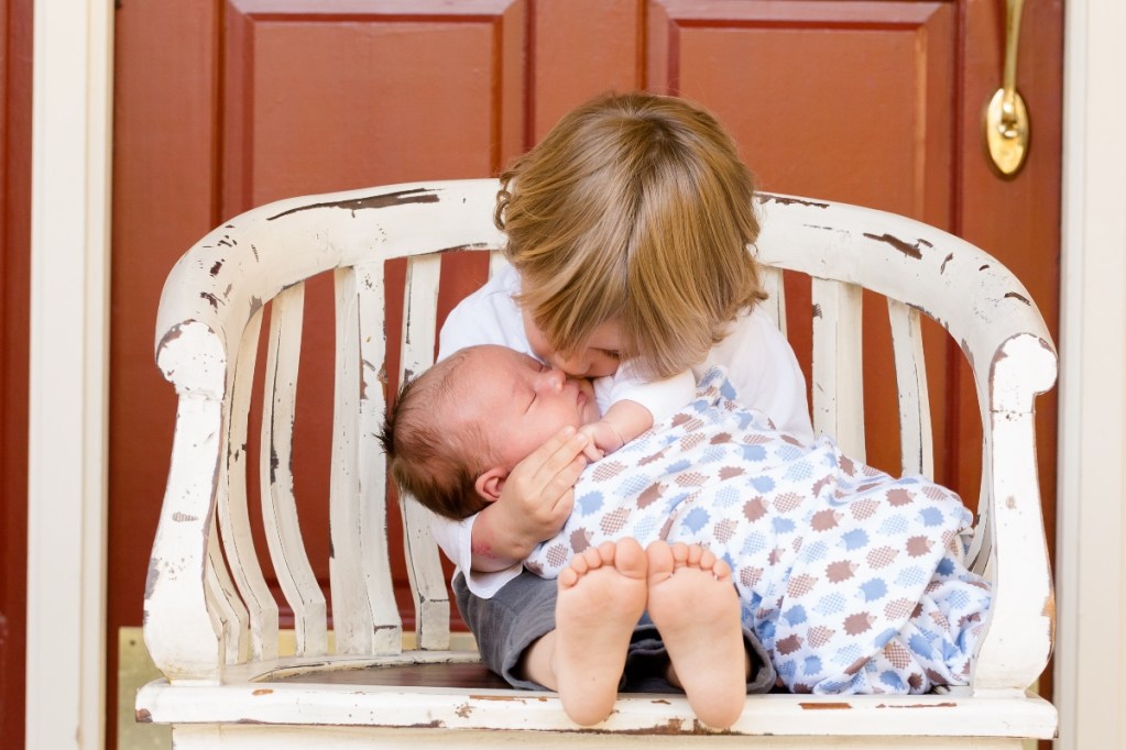 A toddler holding a new baby on a white bench