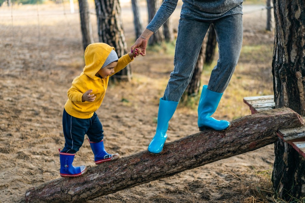 A toddler on a log with a parent.