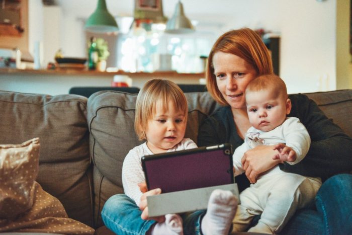 A mother holding her children while looking at a tablet