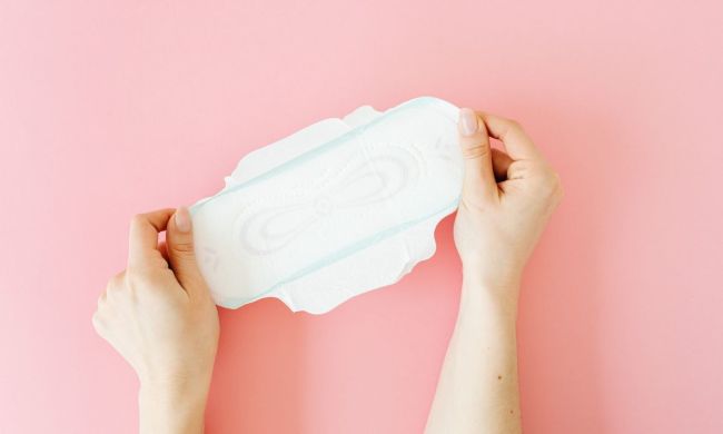 A menstrual pad being held on a pink background