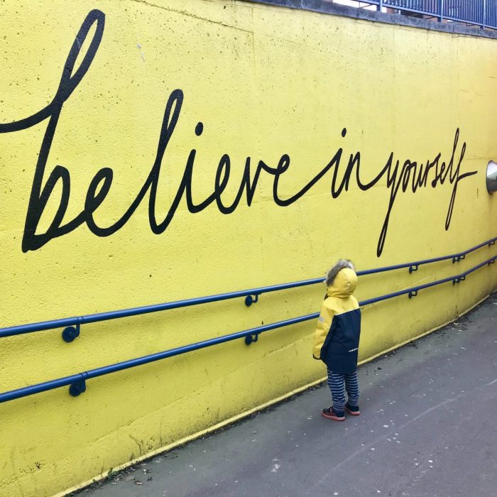 A child looking up at an affirmation written on a wall outside