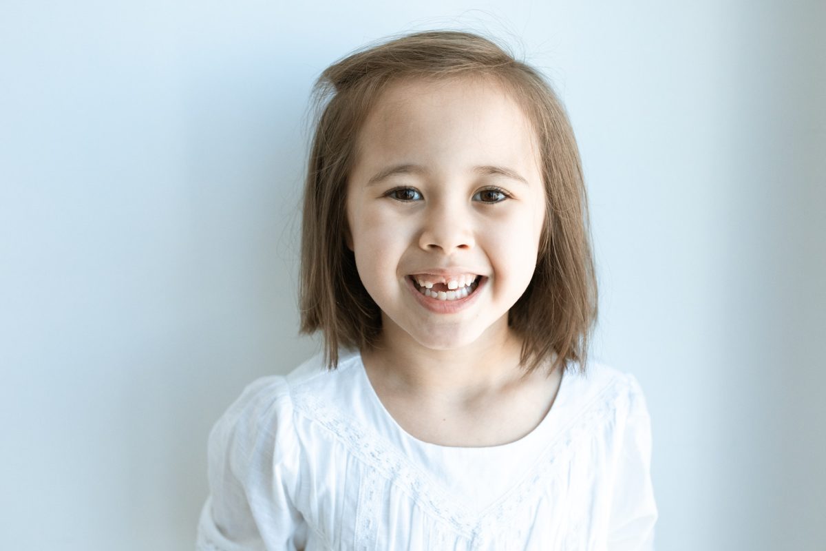 A child smiling, revealing that they are missing a tooth.