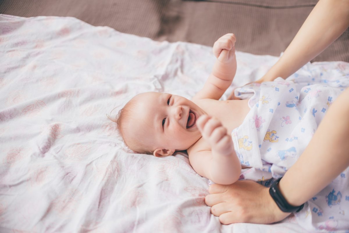 A baby on the bed with a parent making sure they don't fall off.