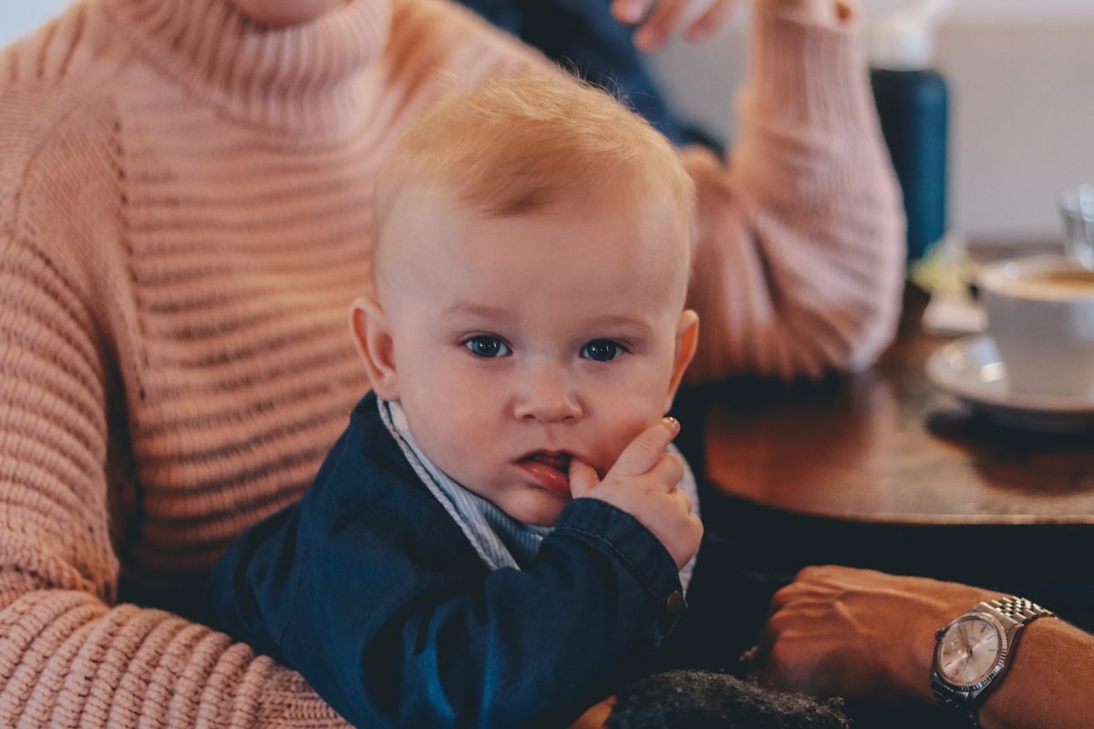A baby sitting in his parent's lap while chewing on his thumb.