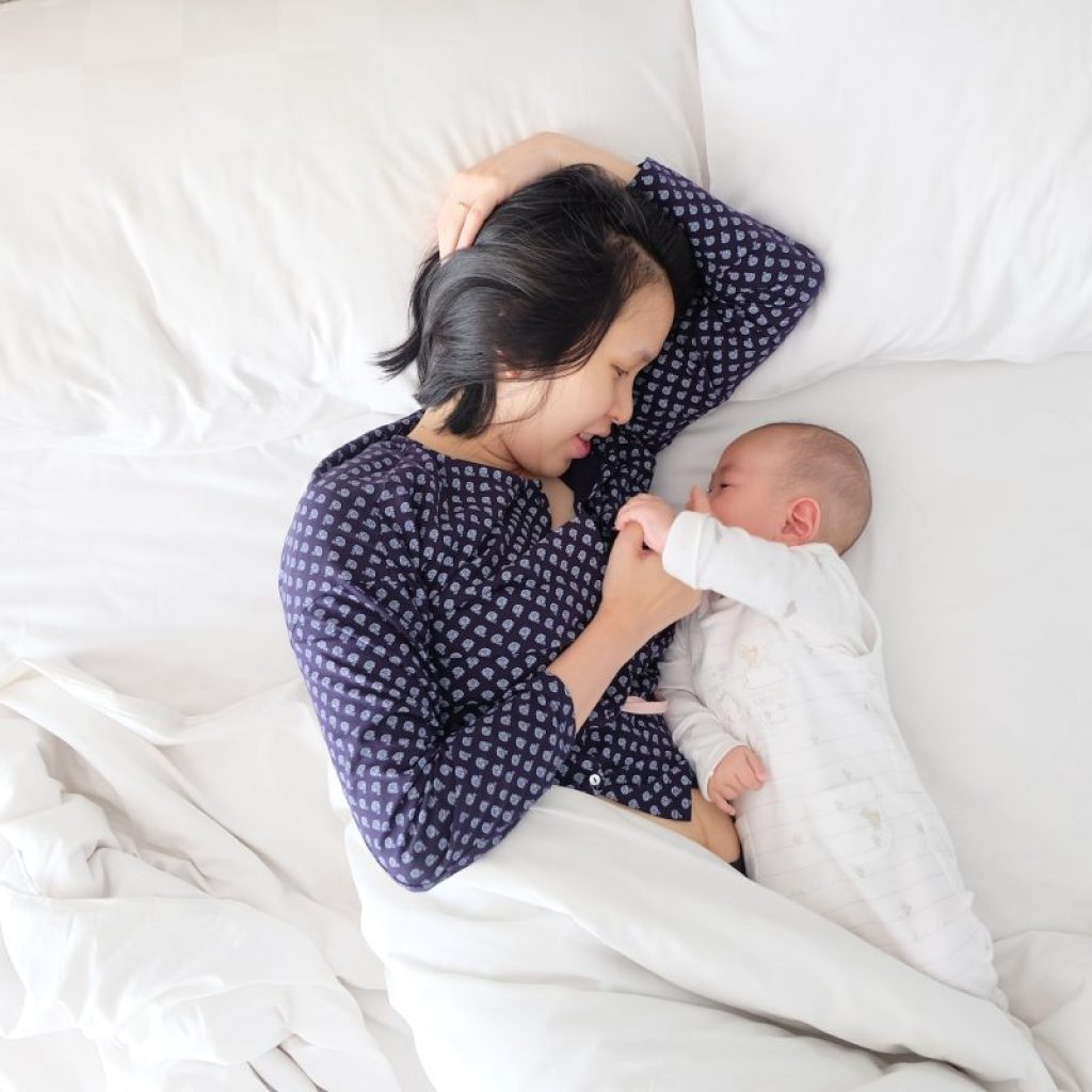 A mother and baby facing each other in the bed.