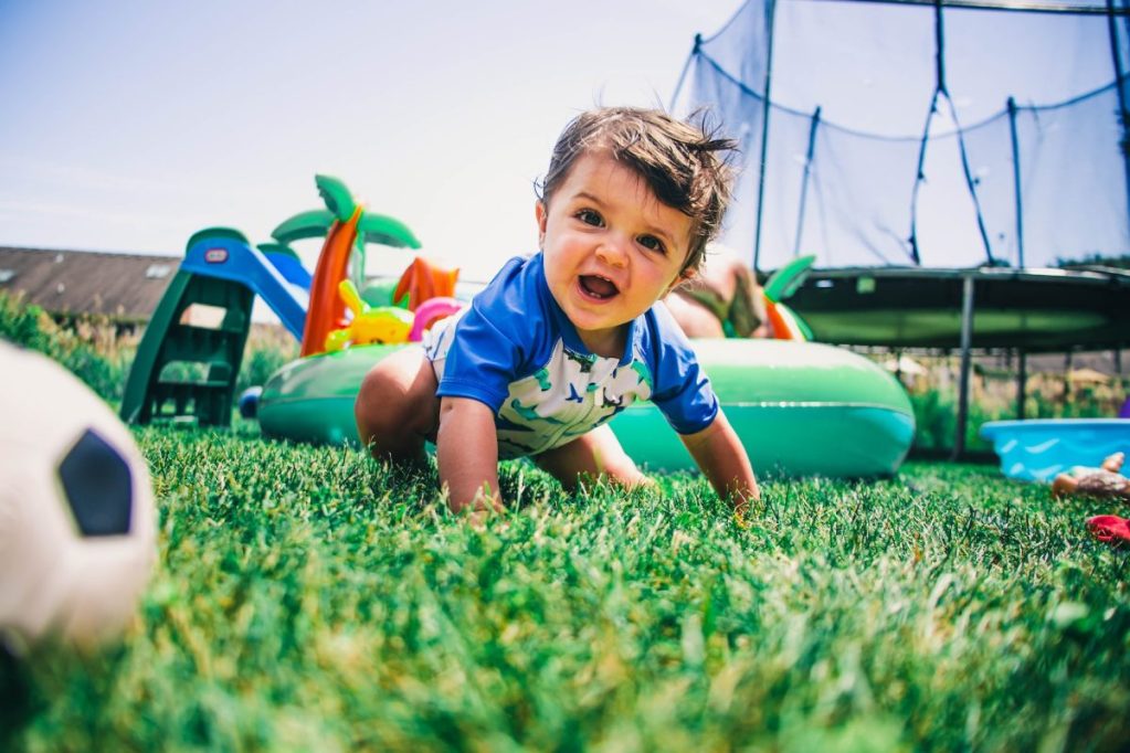 A baby playing outside surrounded by sports equipment.
