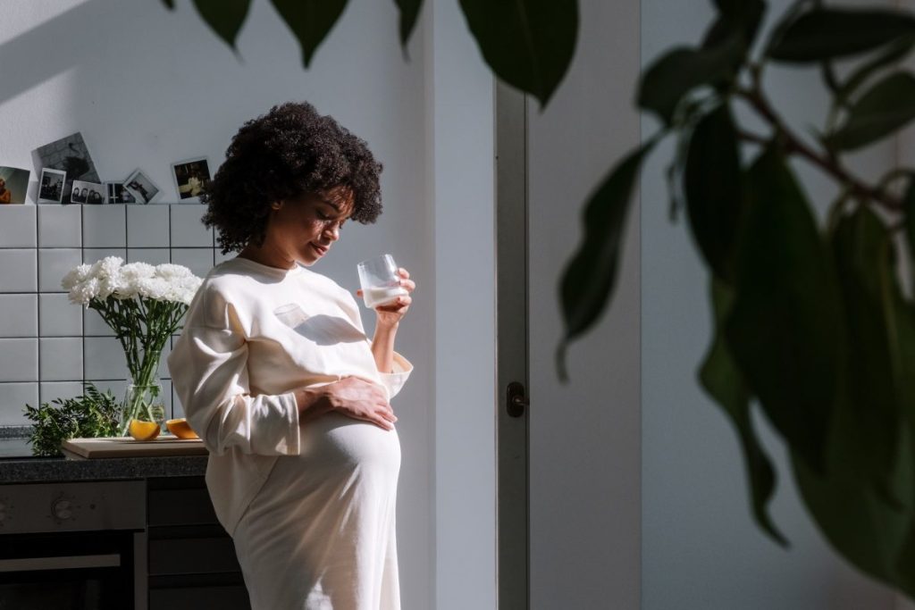 A pregnant woman holding her belly and a glass of water.