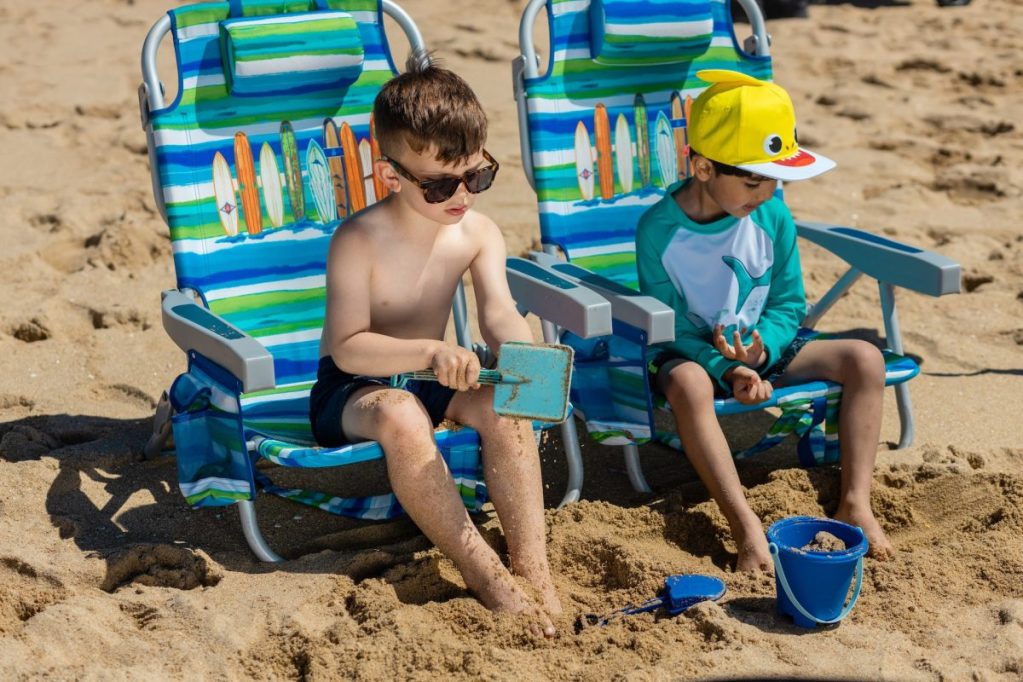 Kids sitting on beach chairs in the sand.