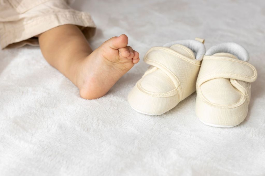 a bare baby foot next to a pair of baby shoes