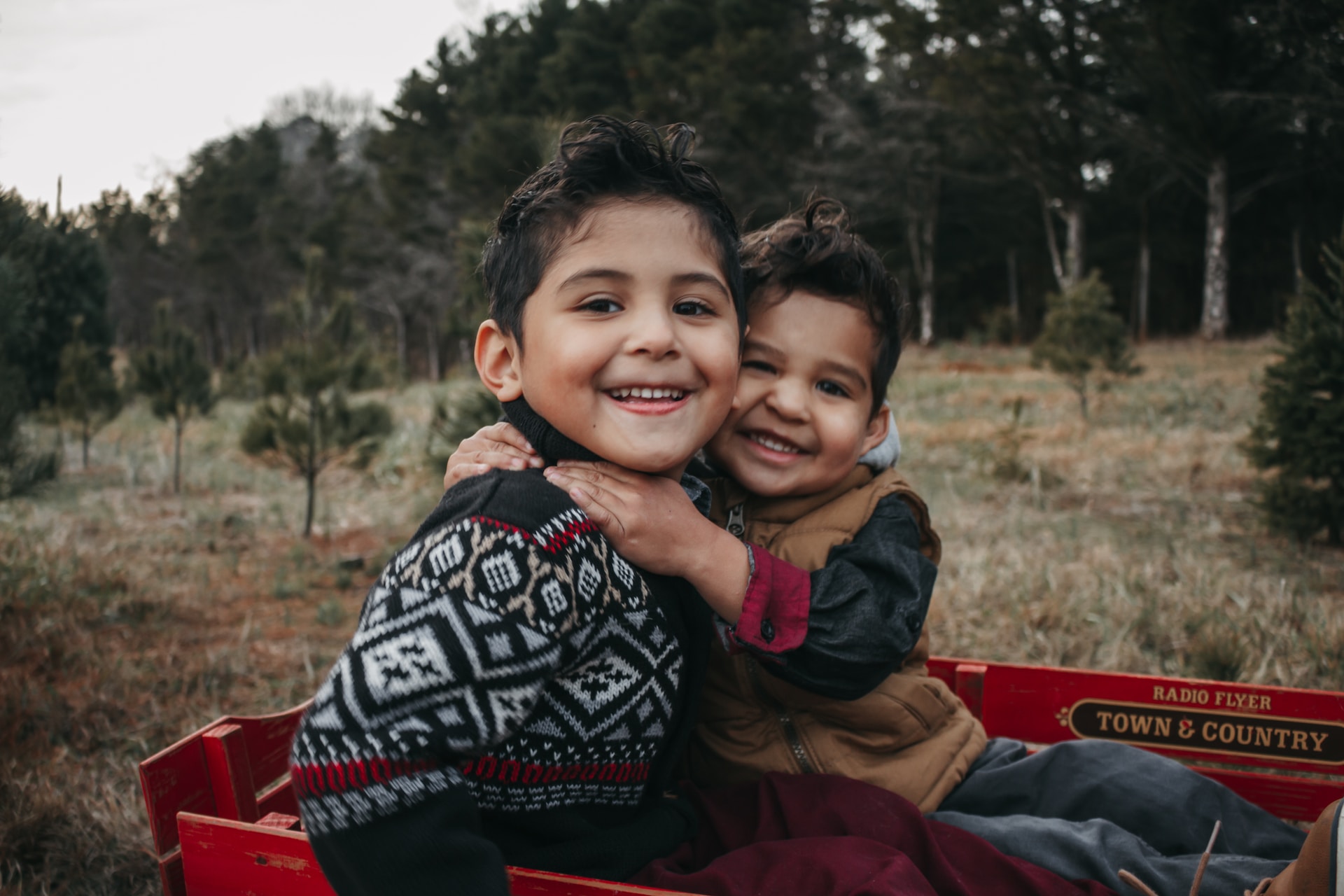 Children in Christmas sweaters sitting in a wagon outside.