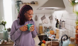 Smiling woman having coffee in kitchen using phone to monitor her sleeping baby