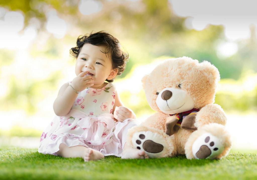 toddler girl sitting on grass with stuffed bear