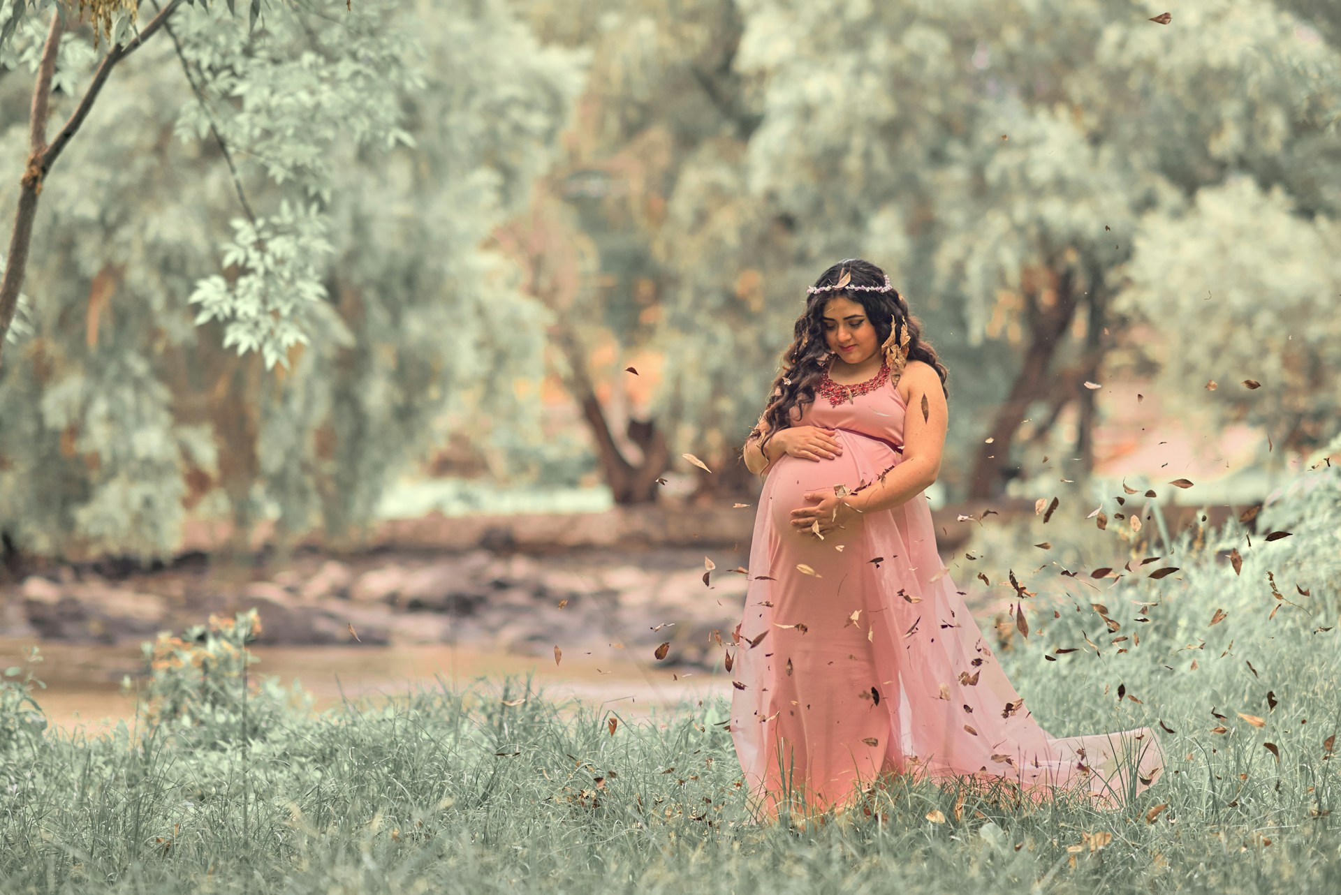A pregnant woman outside wearing a flowing dress and headpiece.