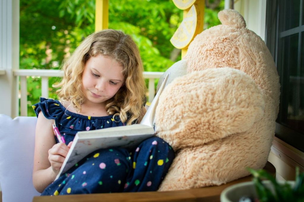 Cute little girls writing in her journal with her teddy bear