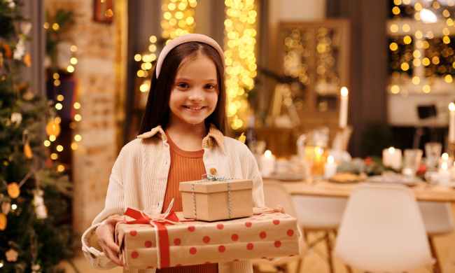 A young child with a white headband holding holiday gifts