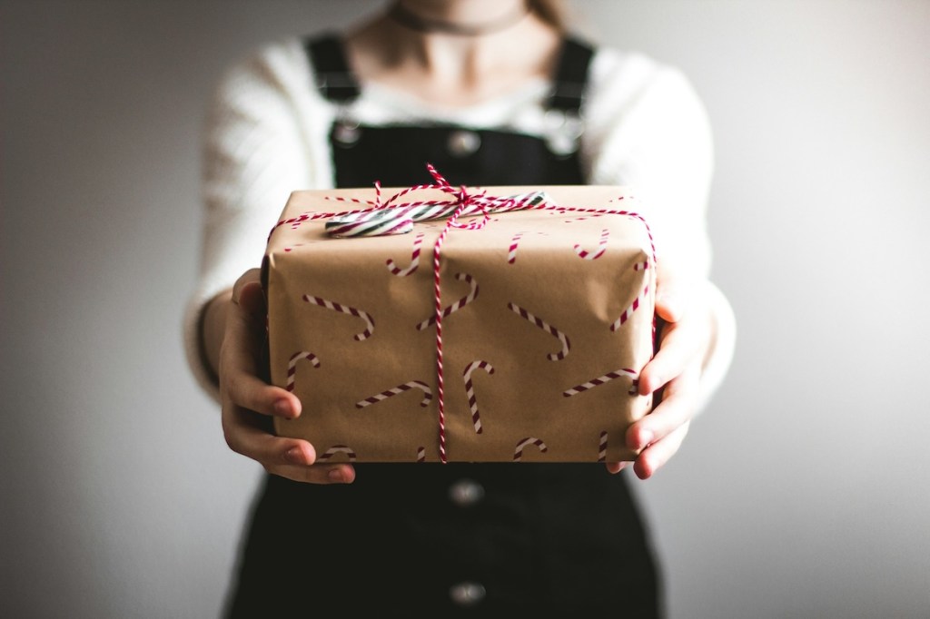 a person holding out a gift wrapped in brown paper with candy canes