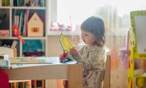 A small girl sitting at a wooden table cutting paper