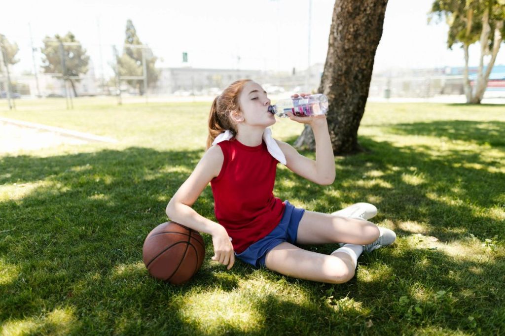 girl drinking water in the shade after basketball practice